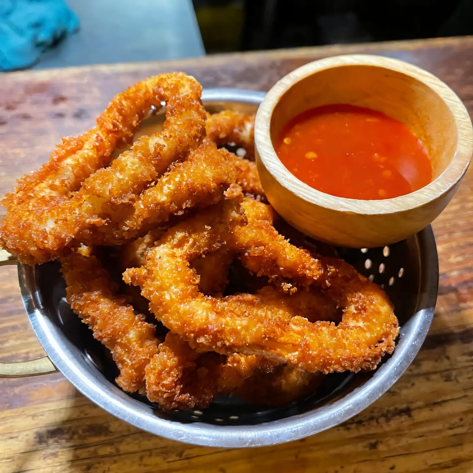Crispy fried calamari rings in a metal colander with a side of sweet chili sauce.