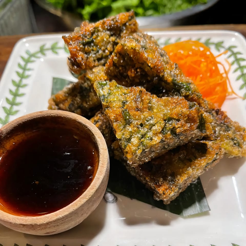 Crispy fried chive cakes with a side of dark dipping sauce and shredded carrots on a white plate.
