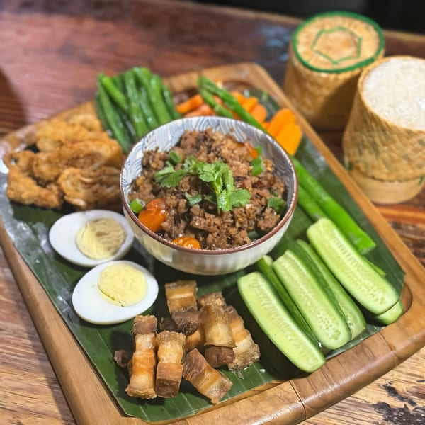 A Thai meal with minced meat, crispy pork, vegetables, boiled eggs, and sticky rice.