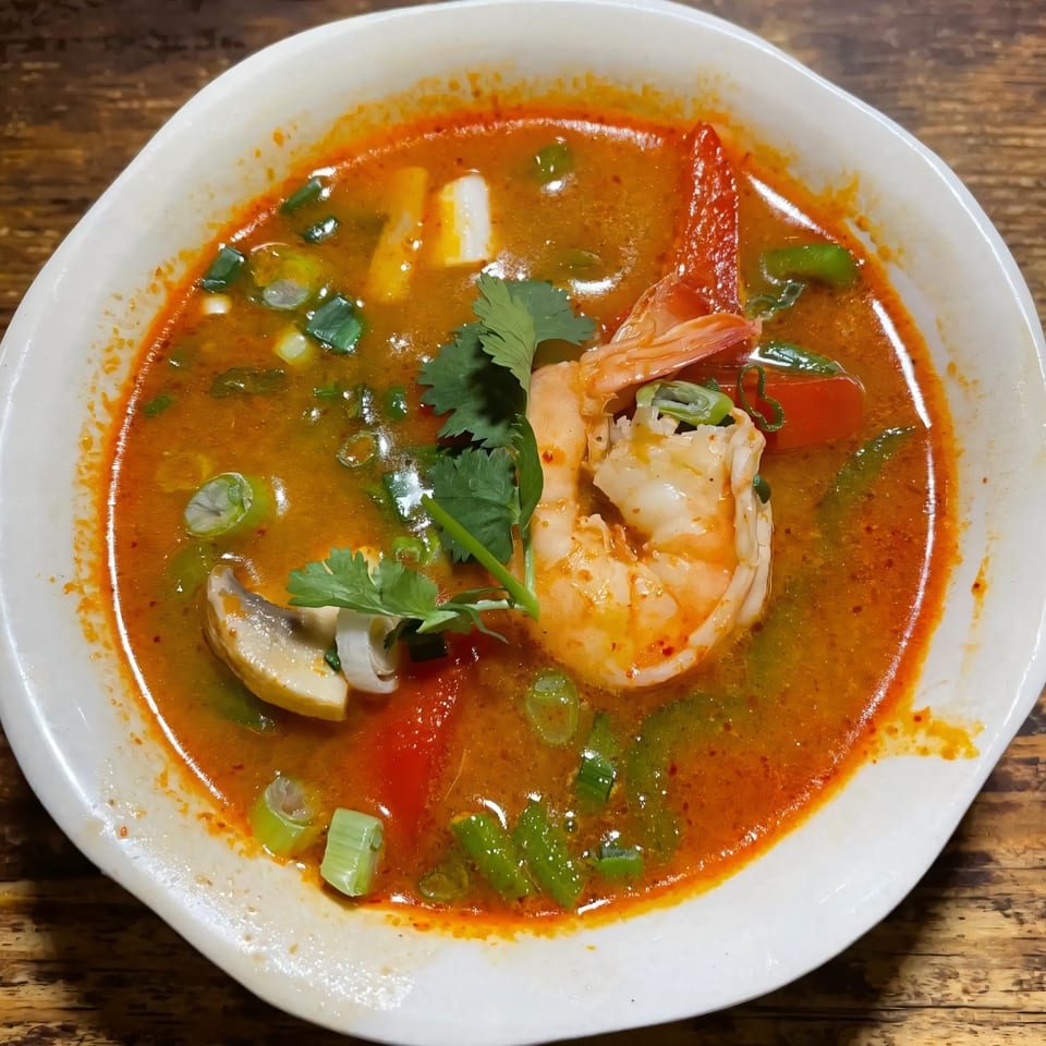 A vibrant bowl of Jintana Thai Farmhouse Tom Yum soup with shrimp, mushrooms, and herbs.