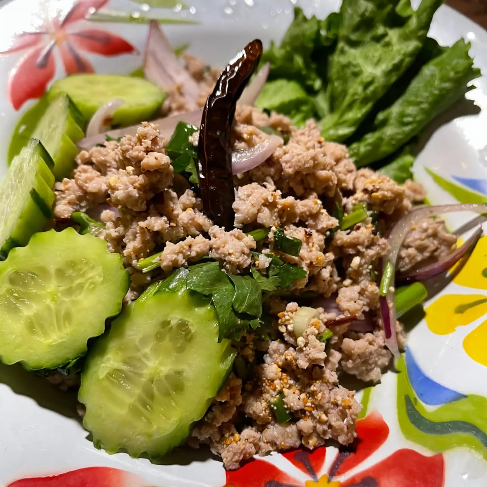 A vibrant Thai larb dish with minced meat, fresh cucumbers, lettuce, and a dried chili.