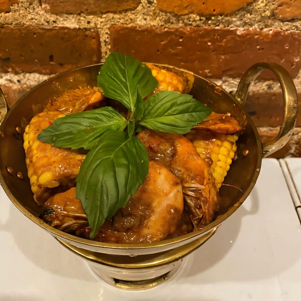 Jintana Thai Farmhouse's shrimp and corn in a rich sauce, garnished with fresh basil in a brass pot.