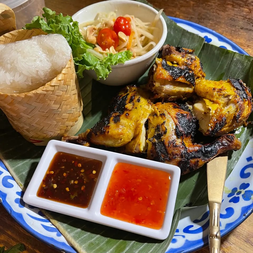 Grilled Thai chicken with sticky rice, papaya salad, and two dipping sauces on a banana leaf.