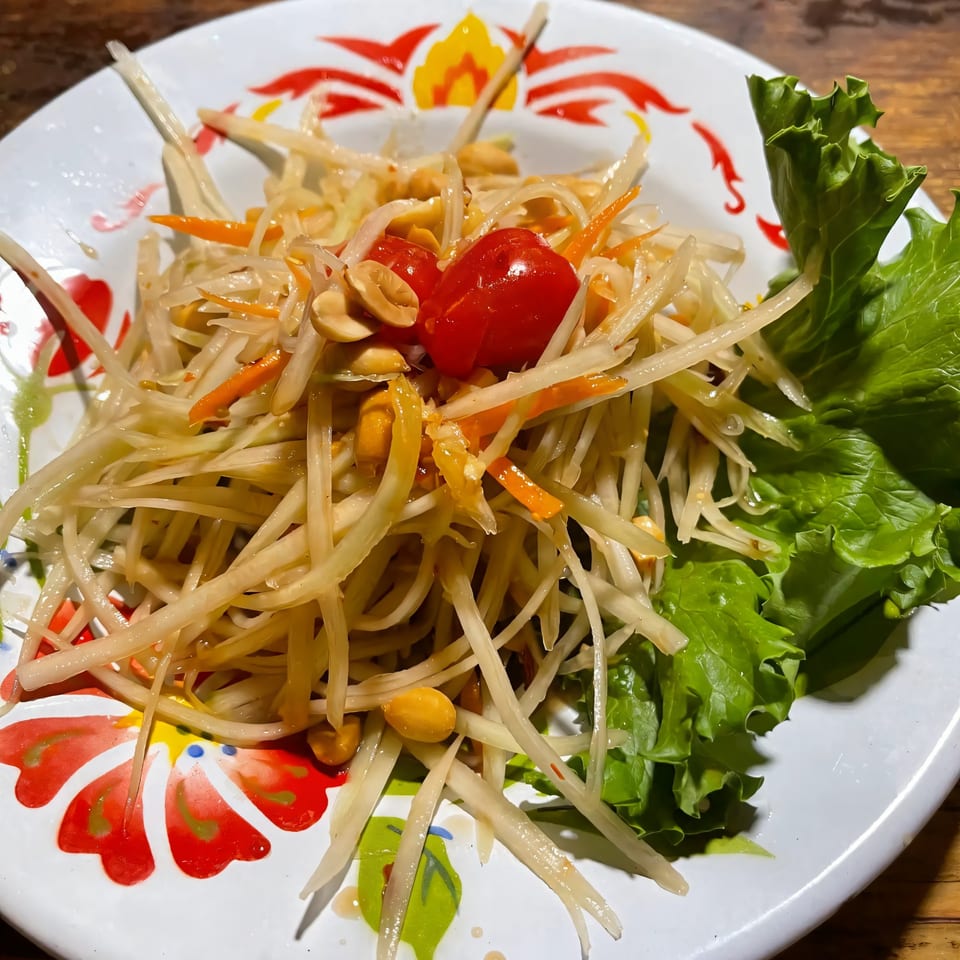 Close-up of Jintana Thai Farmhouse's Som Tum (papaya salad) with tomatoes, peanuts, and lettuce.